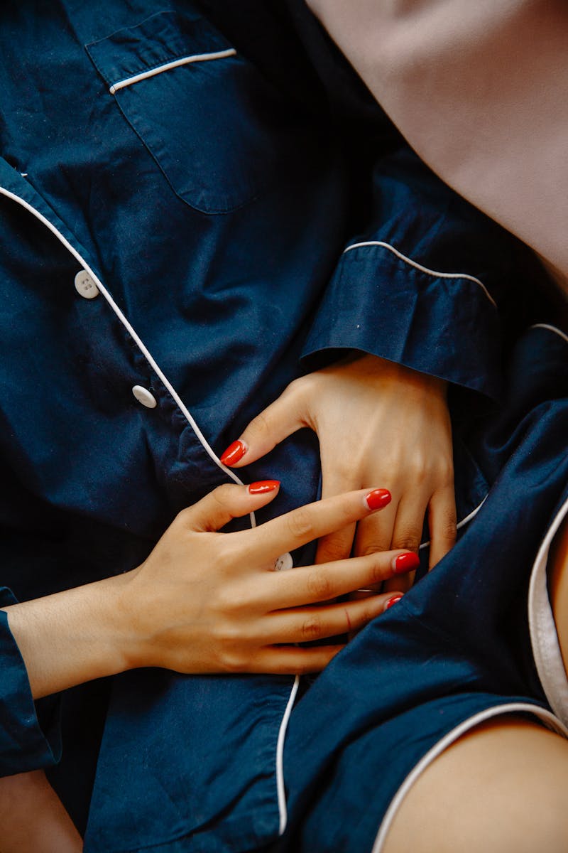 Close-up of a woman in pajamas with hands on her stomach, indicating pain or discomfort.